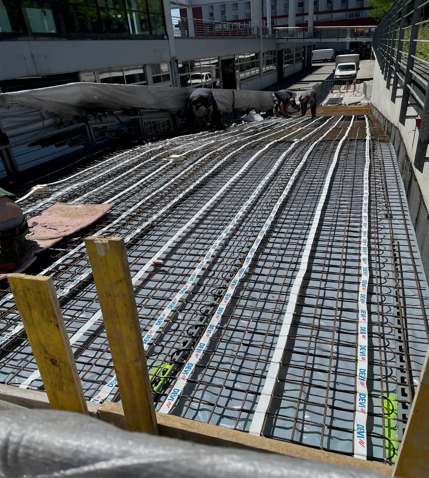 Two installers fastening heating cable to reinforcement mesh on a ramp before the pour.