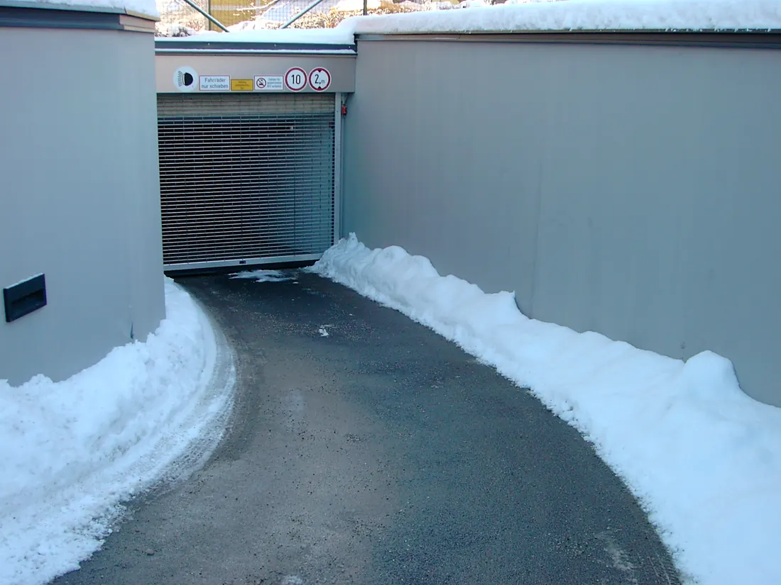 A wet but snow free ramp running down to a garage door between banked snow.