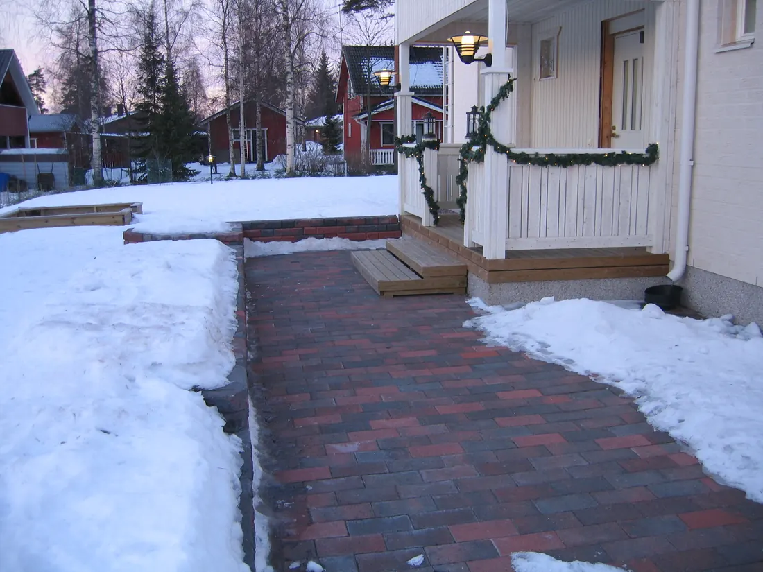 A paved walk to a house door held clear of snow, with snow lying on the ground on both sides.