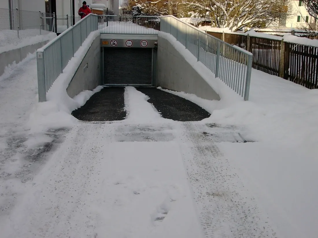 A snow covered ramp with two cleared strips running down it where the heated tire tracks are.