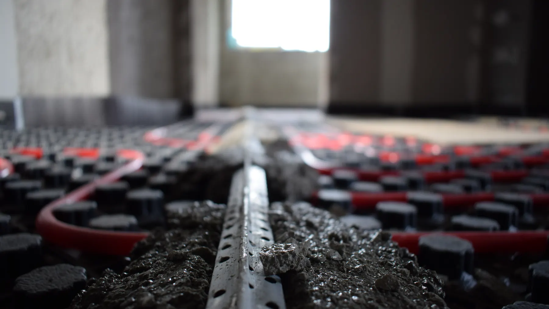 A low view along a slab under construction, the run held on fixing strip and studded panel as the pour goes down over it.