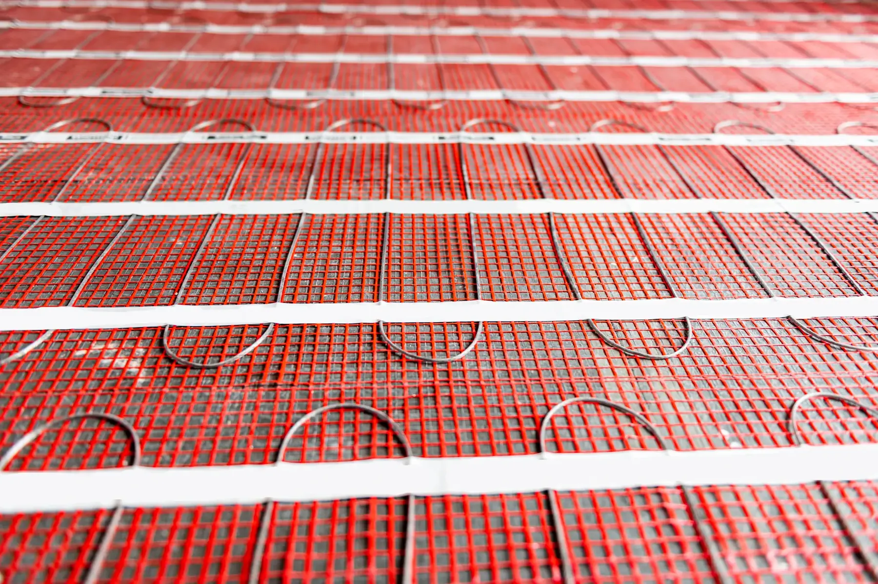 Electric heating mat taped down over a floor, the cable held on a mesh backing in parallel runs before the finish goes on.